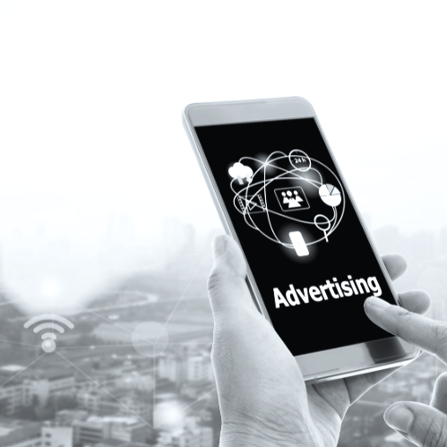 Person holding a smartphone displaying the word 'Advertising' with digital icons and network connections, over a cityscape background.
