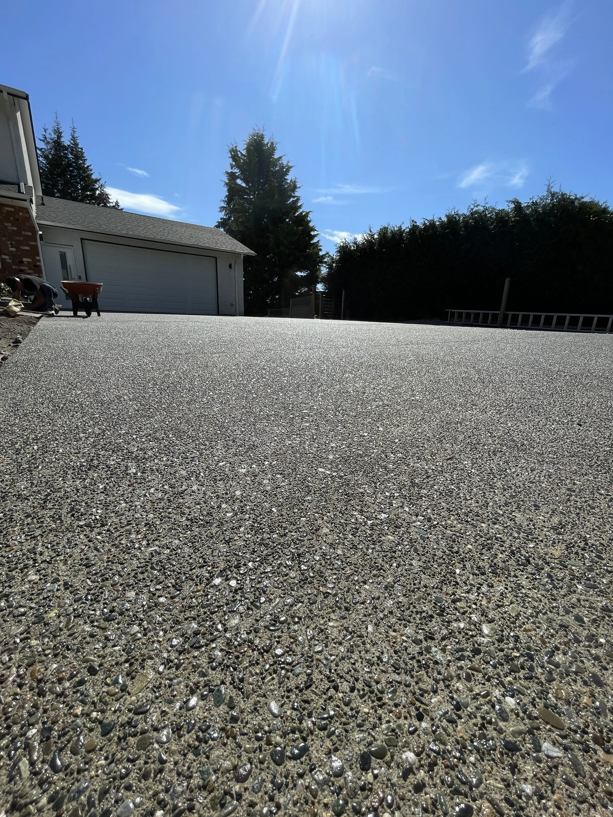 Newly poured concrete driveway with an exposed aggrigate finish in front of a house under a blue sky with sunlight in Brentwood neighbourhood, in Victoria BC.