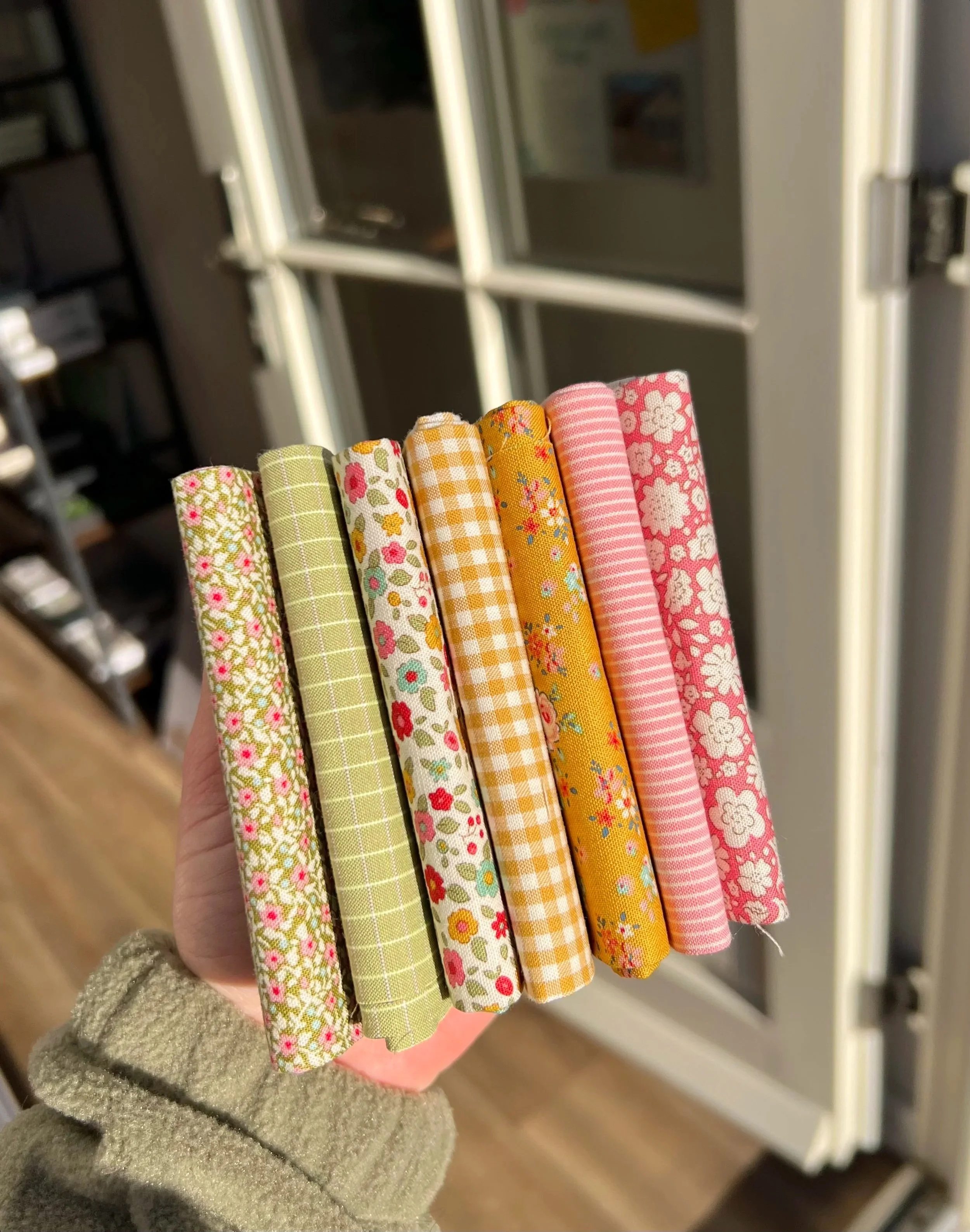 Hand holding a compact stack of colorful patterned fabric swatches with floral, checks, and striped designs.