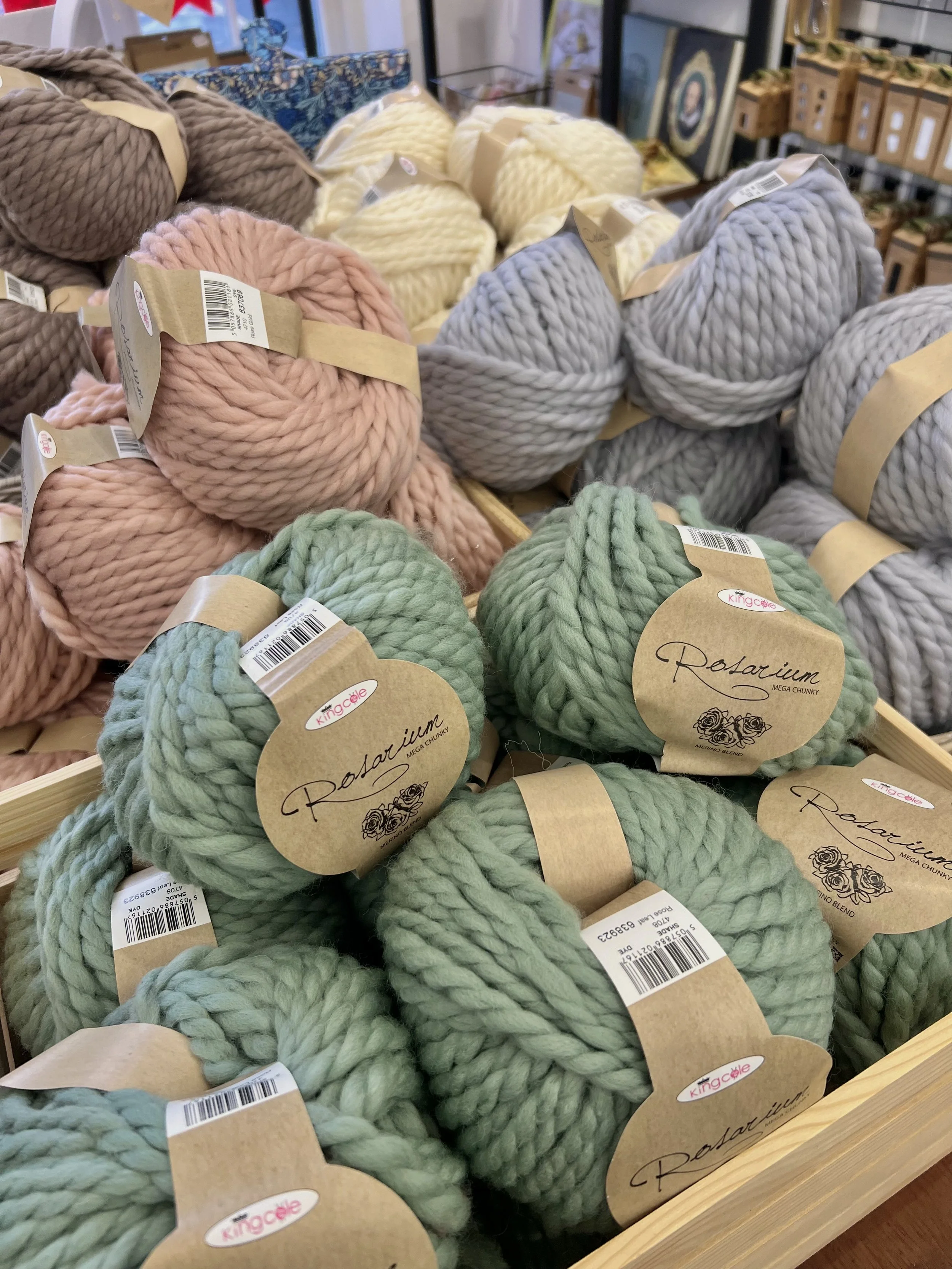 Balls of thick yarn in pink, green, and gray colors displayed in a retail store.