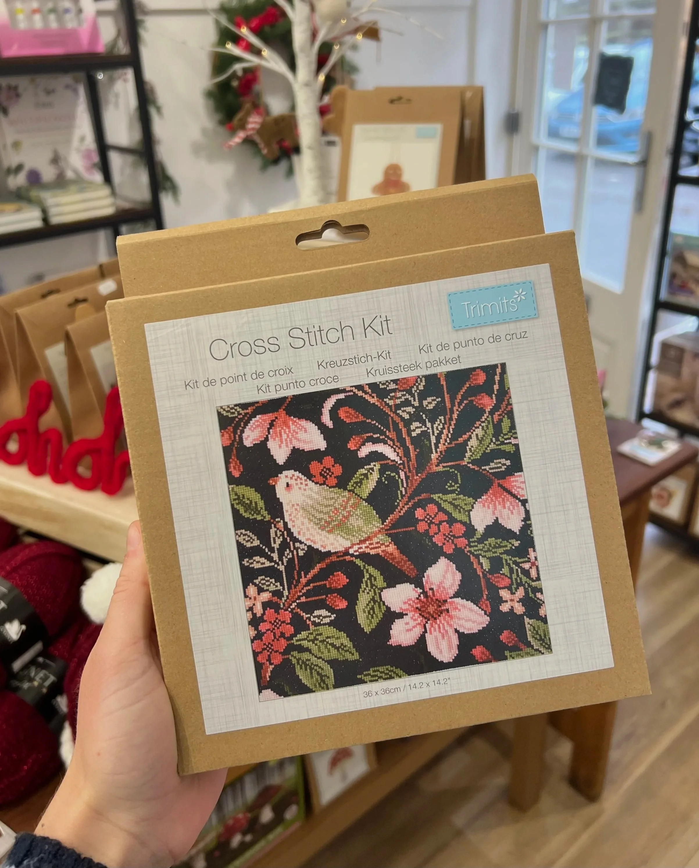Cross stitch kit featuring a bird sitting on a branch with pink flowers and green leaves, set against a black background.
