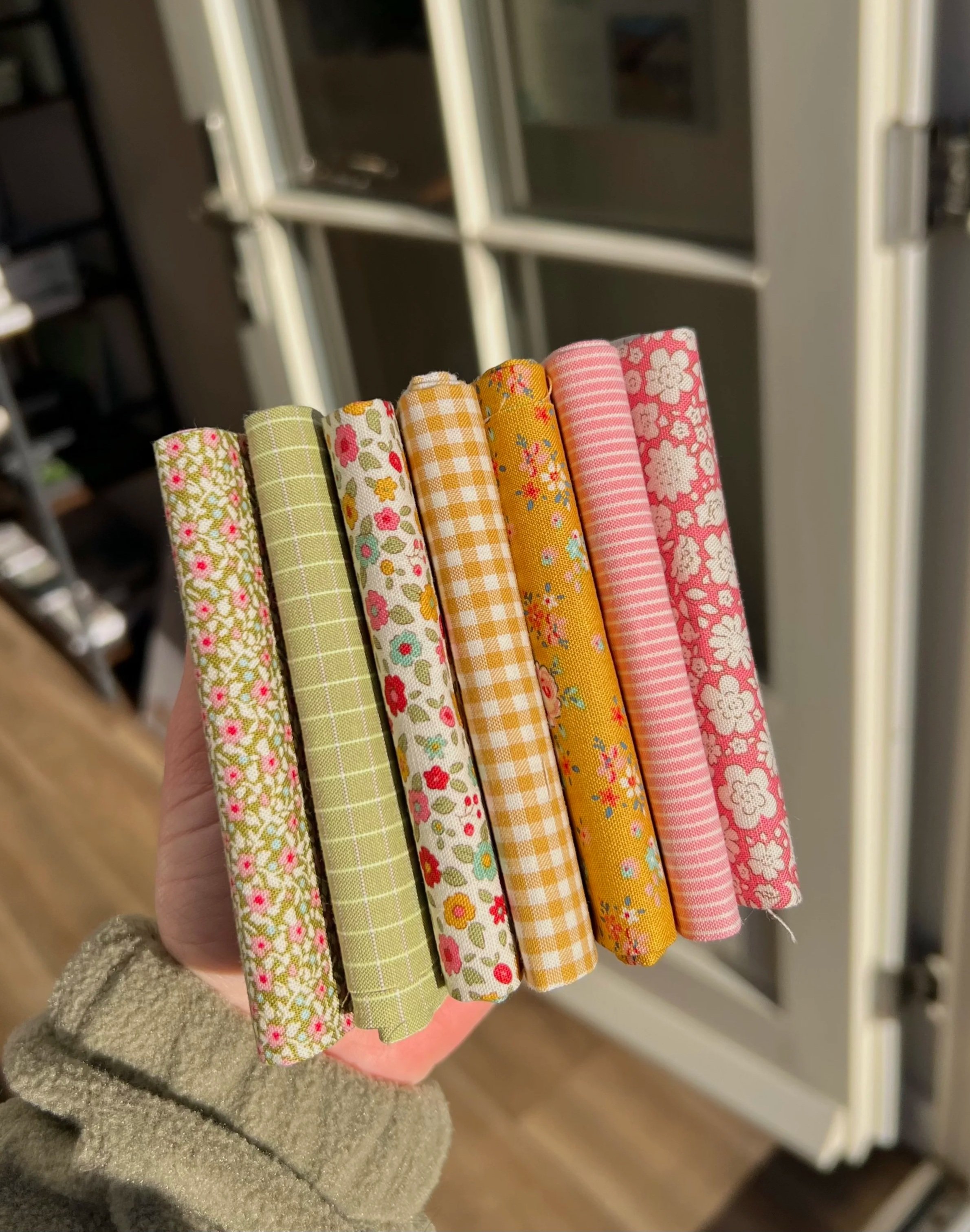 Hand holding a collection of eight colorful fabric rolls with floral and checkered patterns.