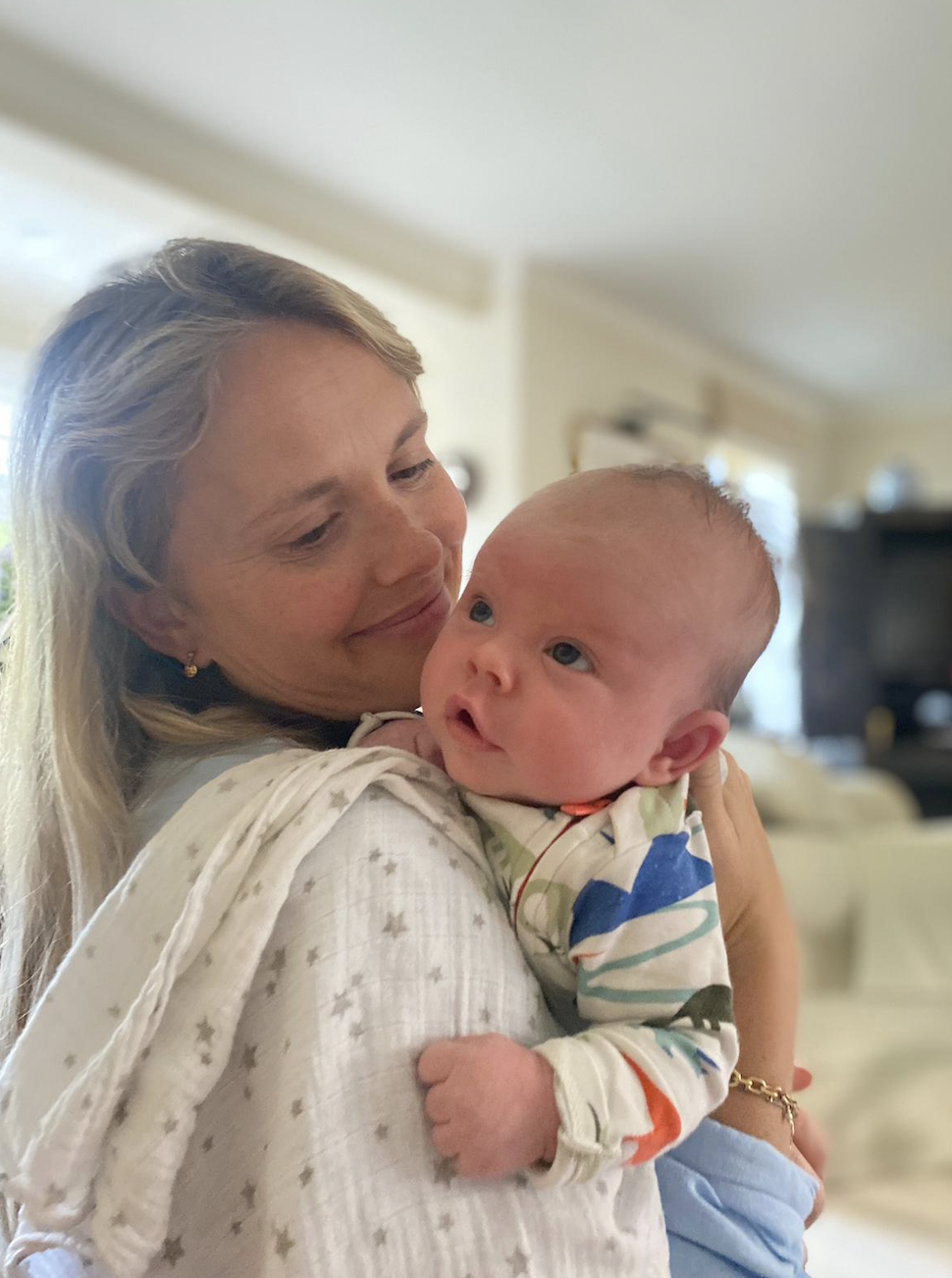 A woman holding a baby in a cozy home interior with a blurred background.