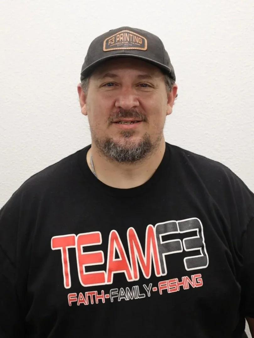 A man with a beard and mustache wearing a black T-shirt that says "TEAM F3" with the words "FAITH, FAMILY, FISHING" underneath, and a gray cap with a patch that reads "PRINTING ADULT 2.0TX".