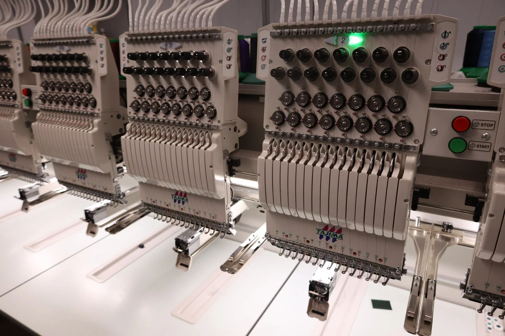 Close-up of industrial embroidery machines with multiple spools of thread, working in a factory setting.
