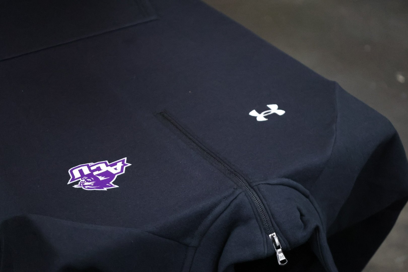 A black Under Armour backpack with the AACU logo and an Under Armour logo on it.