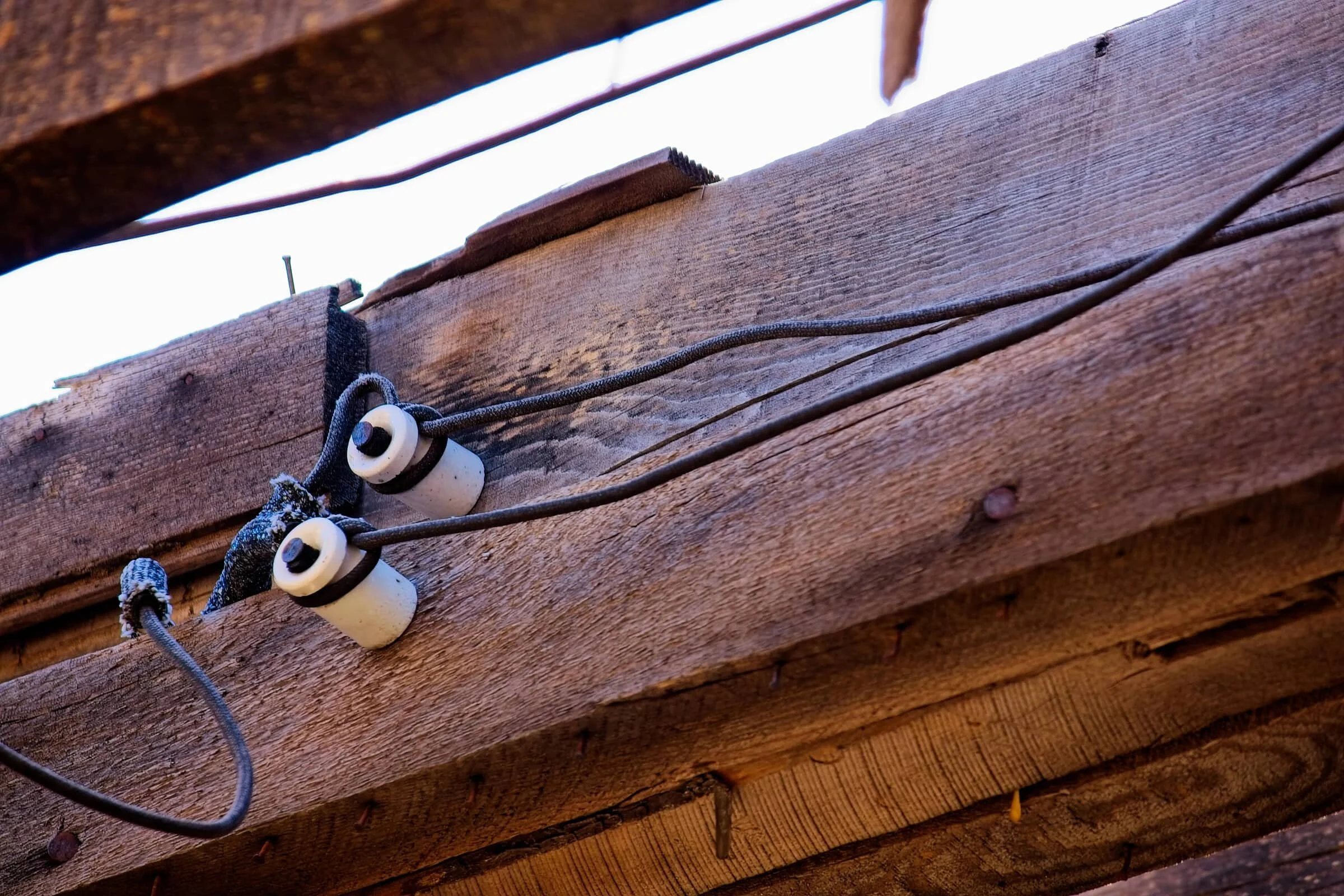 Close-up of a wooden outdoor structure, possibly a fence or support beam, with electrical wires and insulators attached.