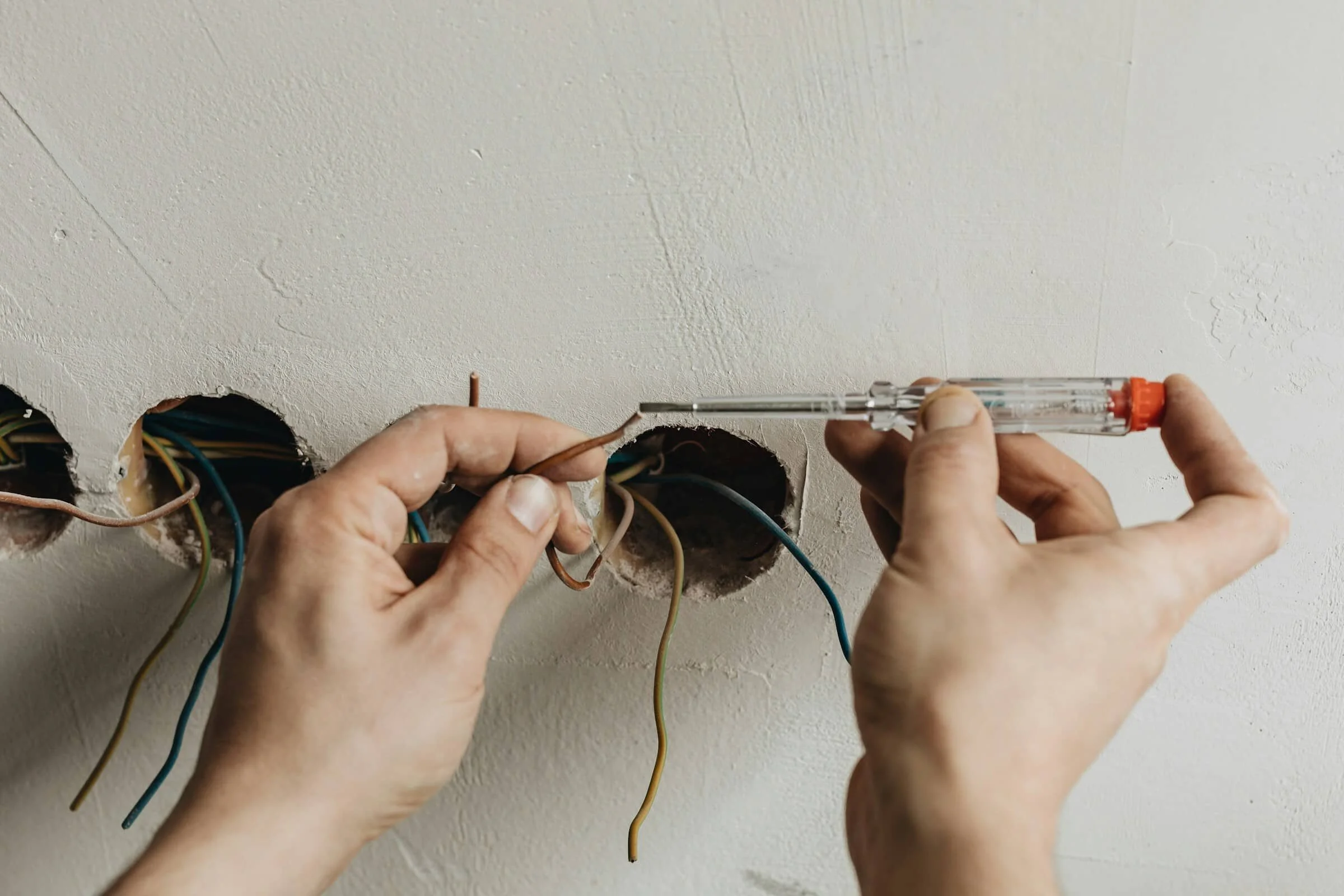 Person working on electrical wiring in wall, using screwdriver to connect wires into an electrical box.