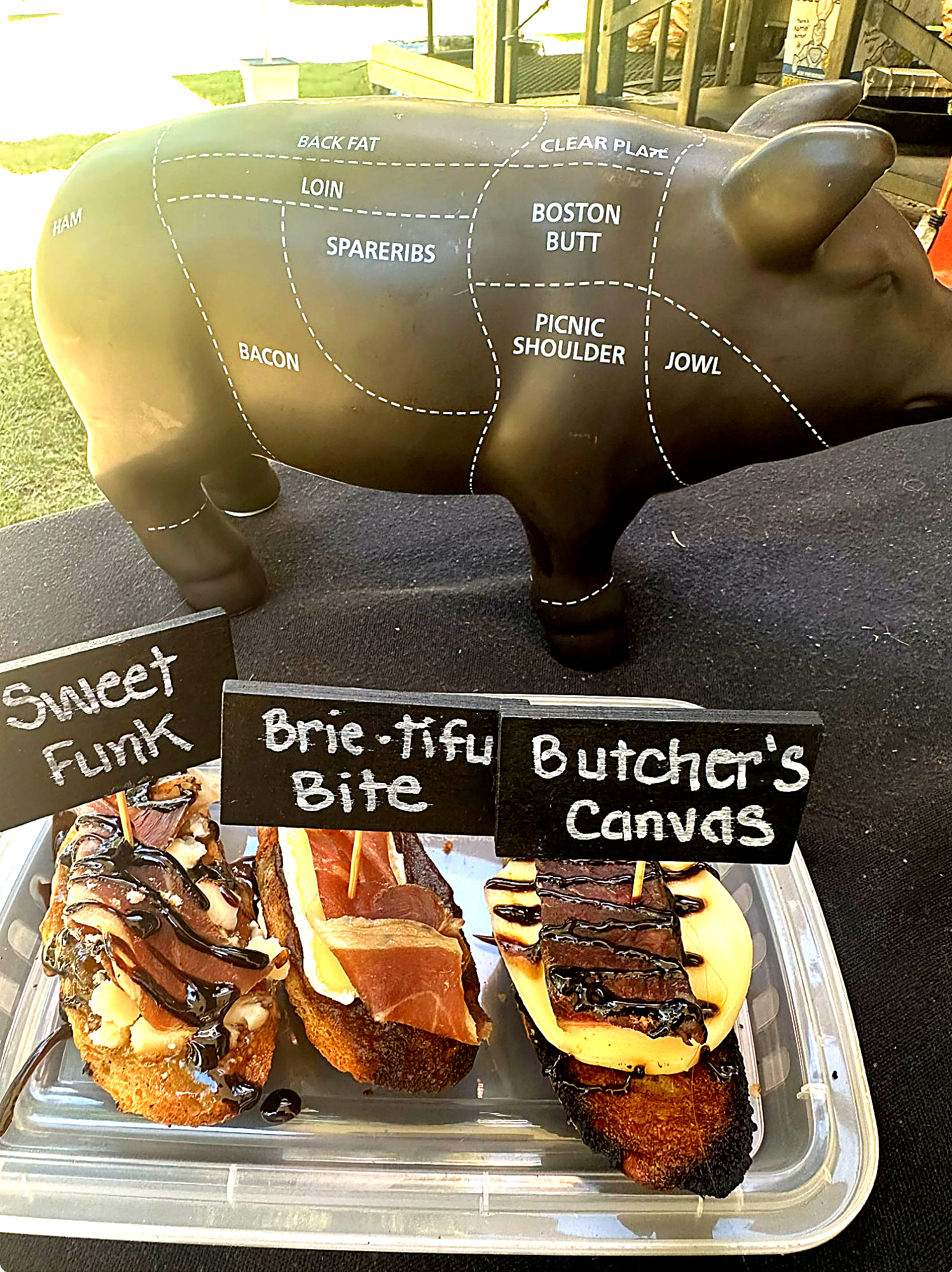 A pig-shaped diagram with labeled sections for different cuts of meat, and three open-faced sandwiches on a tray below labeled 'Sweet Funk,' 'Brie Tifu Bite,' and 'Butcher's Canvas.'