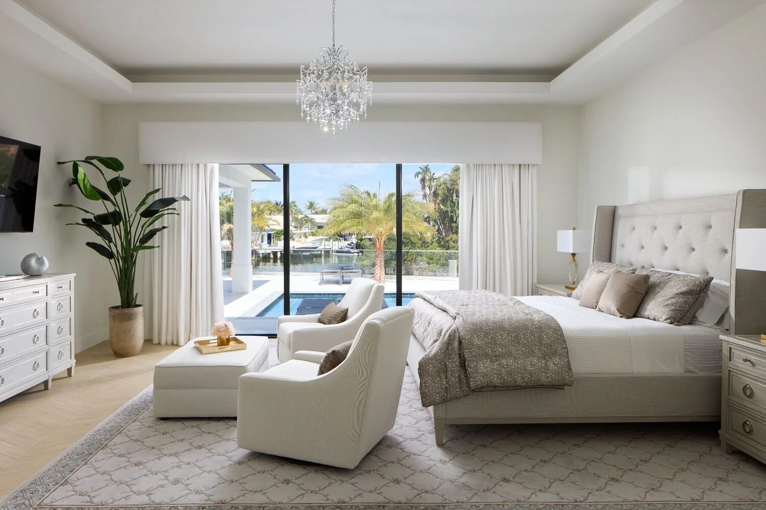 Coastal primary bedroom with layered neutral bedding, chandelier lighting, and soft natural textures