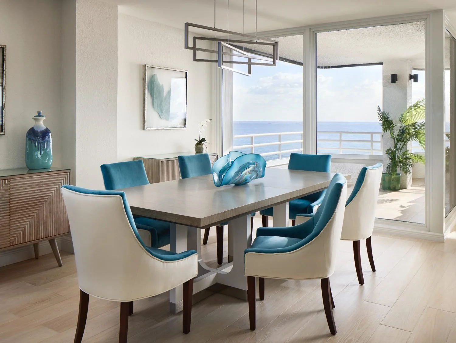 Oceanfront dining room with modern chandelier, coastal palette, and expansive water views