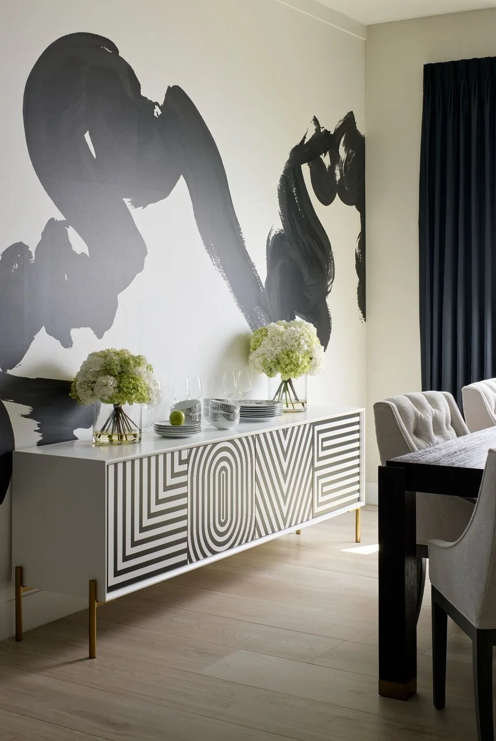 Dining room design with abstract black-and-white wall mural, LOVE patterned console, and modern upholstered dining chairs