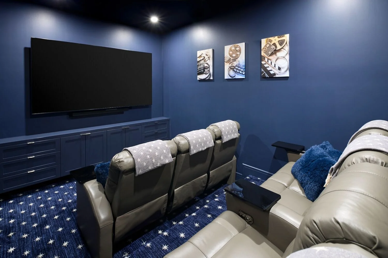Home theater design with navy walls, built-in media cabinetry, oversized screen, and leather recliner seating