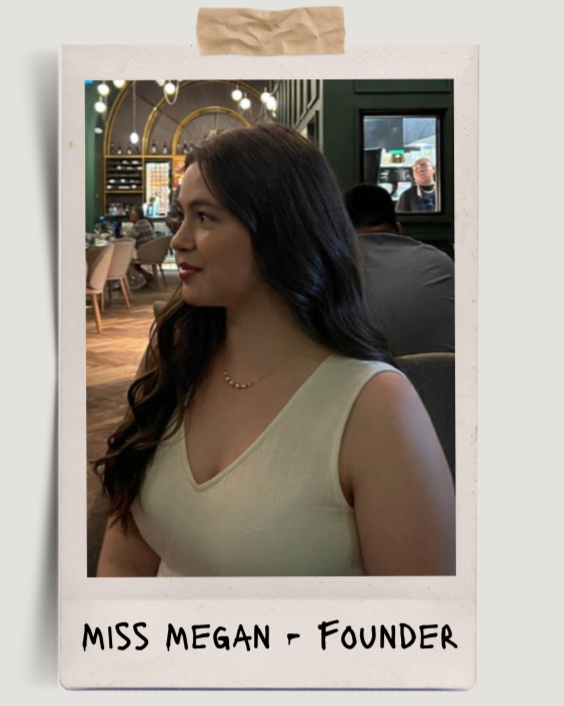 A young woman with long, dark hair and light skin, wearing a cream sleeveless top and a delicate necklace, sitting in a restaurant or cafe with a modern interior, including wooden flooring and decorative lighting.