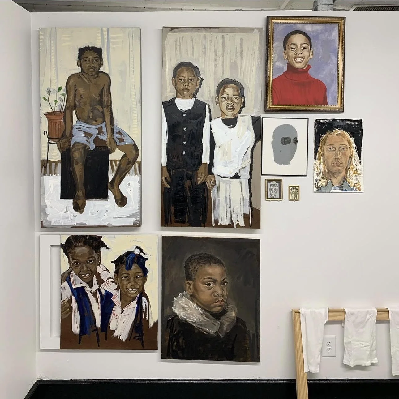 Una pared decorada con varios retratos de niños y adolescentes, en una mezcla de estilos realistas y expresivos, dispuestos sobre una pared blanca.