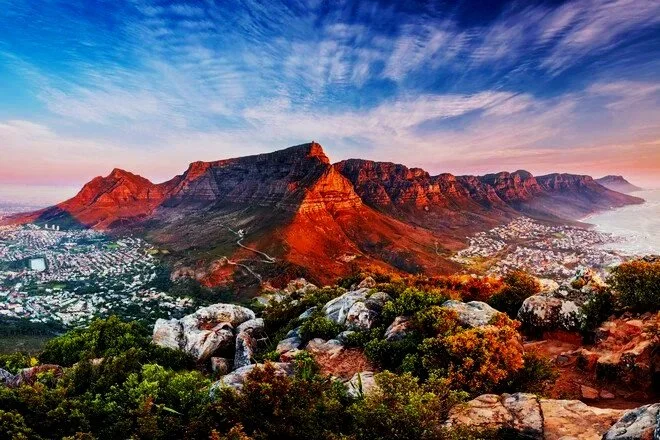 A New Era Africa. Sunrise over the mountains with a town at the base and rocky, green foreground.