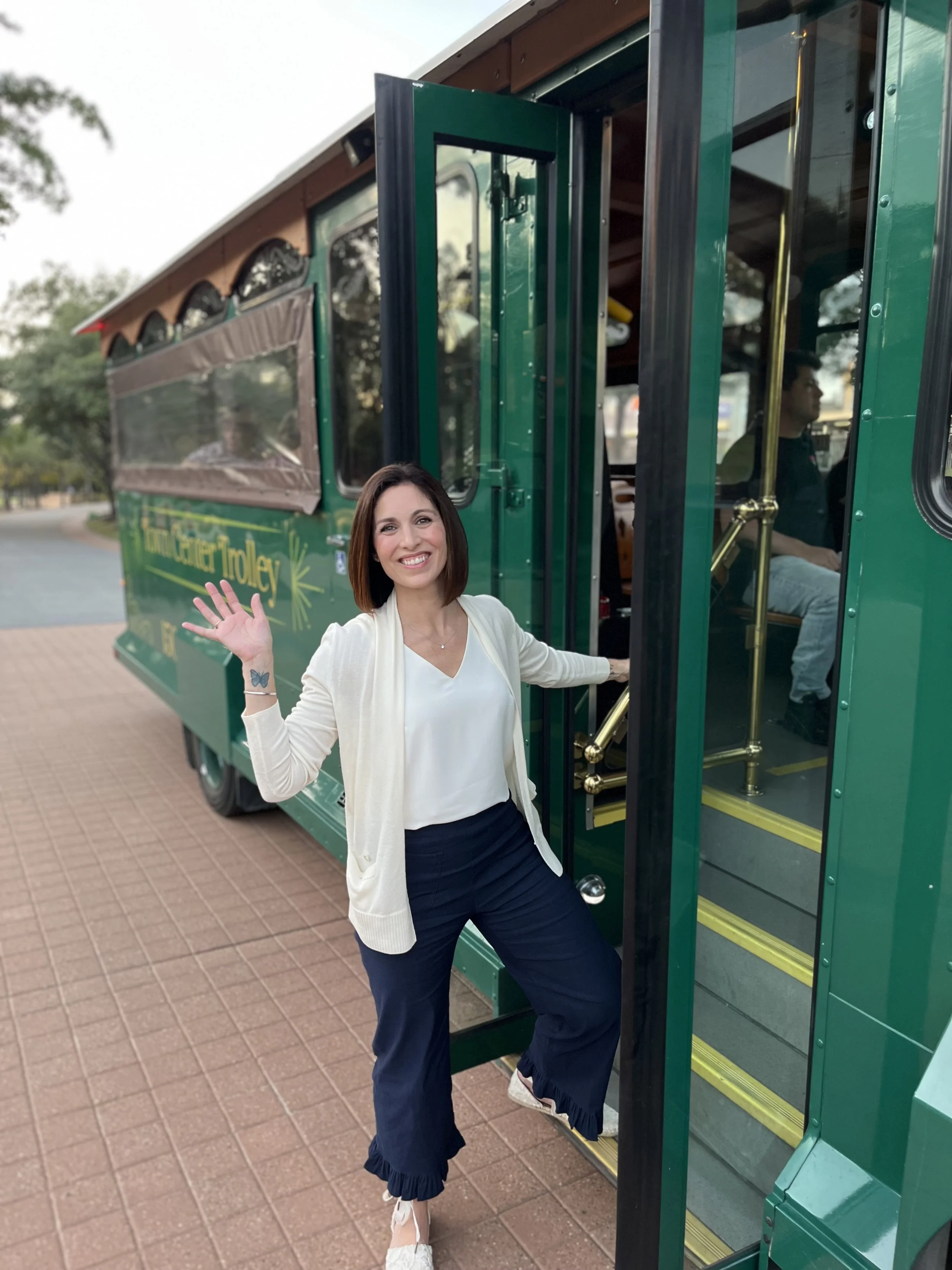 Heather Gallagher, smiling and waving while stepping off a green trolley from The Woodlands, Texas.