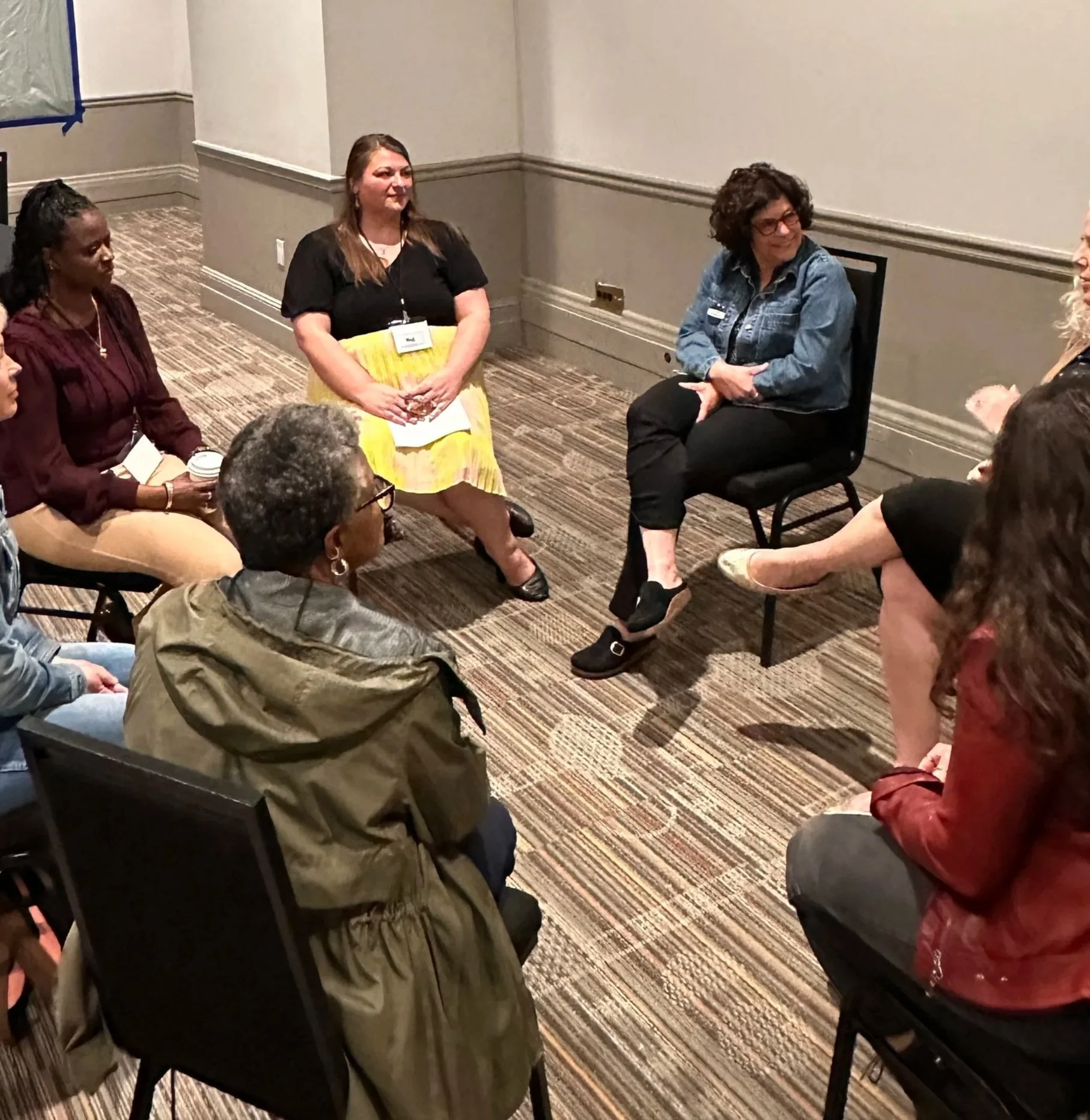 Women seated in a circle in a meeting room, engaging in a discussion.