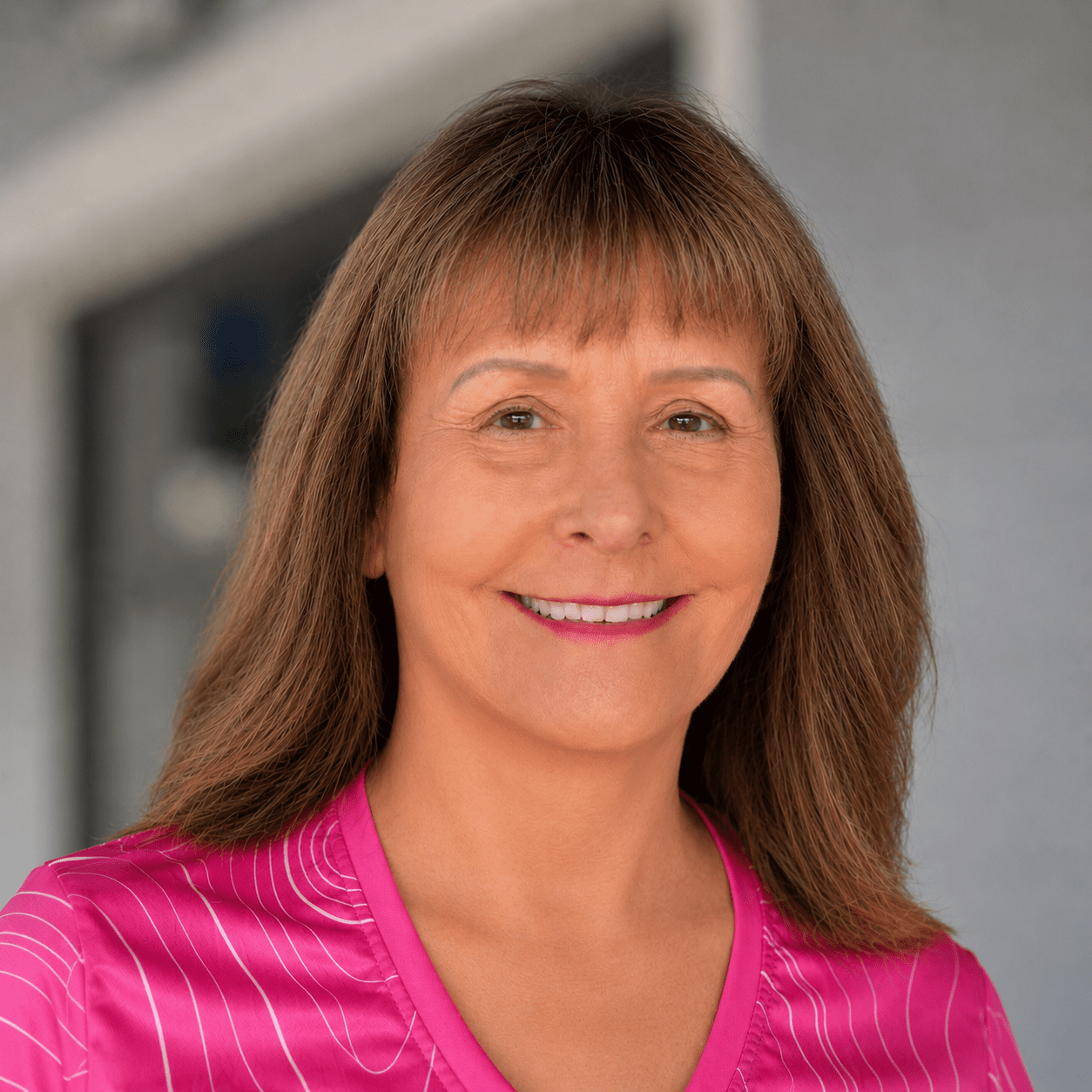 A smiling woman with shoulder-length brown hair wearing a pink striped blouse.