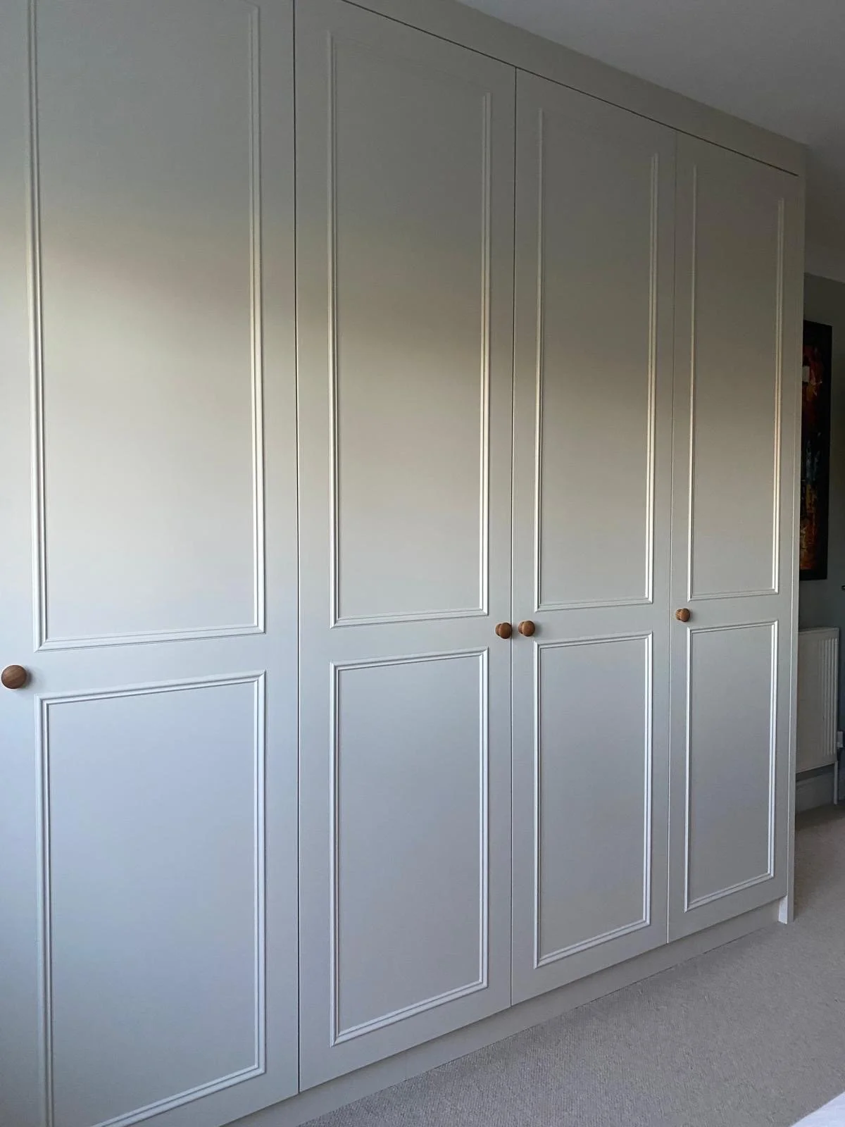 Bespoke victorian wardrobes dressing room with panelled doors and wooden round knobs in a room with carpeted floor.