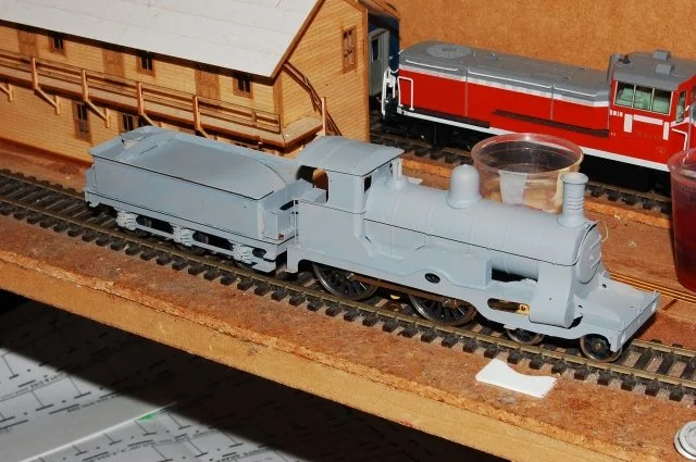 Model train on a track with a wooden building and other model trains in the background.