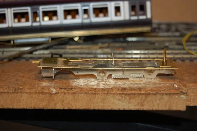 Close-up of a model train decoder placed on a wooden surface with train tracks and electrical components in the background.