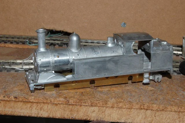 Close-up of a silver model train locomotive on tracks against a brown background.