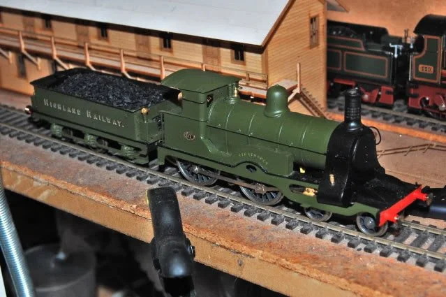 Model train of a green locomotive and coal car on a track.
