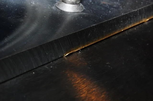 Close-up of a metal saw blade cutting through a black material.