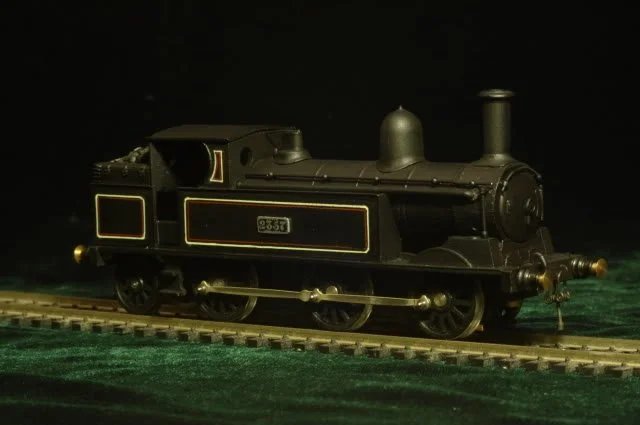 Black miniature steam locomotive on train track against dark background