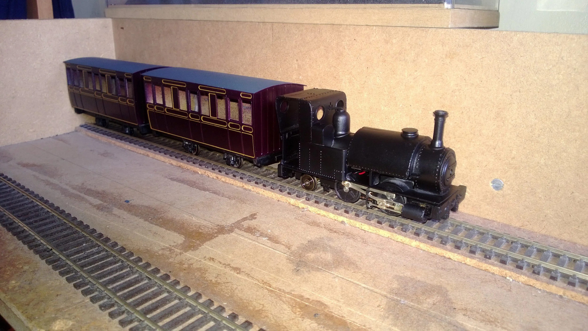 Model train engine and two passenger cars on a track in an indoor setting.