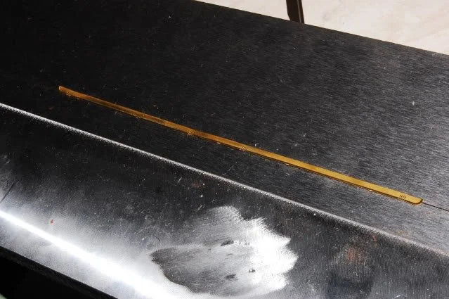 A black wooden surface with a yellow flexible measuring tape and a shiny metallic object with a smudge on it