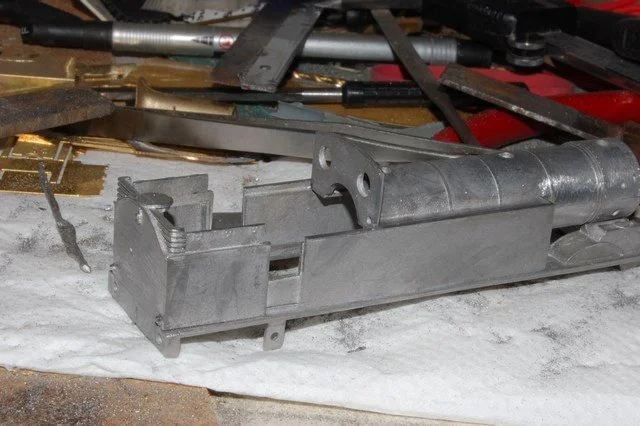 A metal firearm component, possibly a slide or bolt, on a workbench surrounded by tools and equipment.