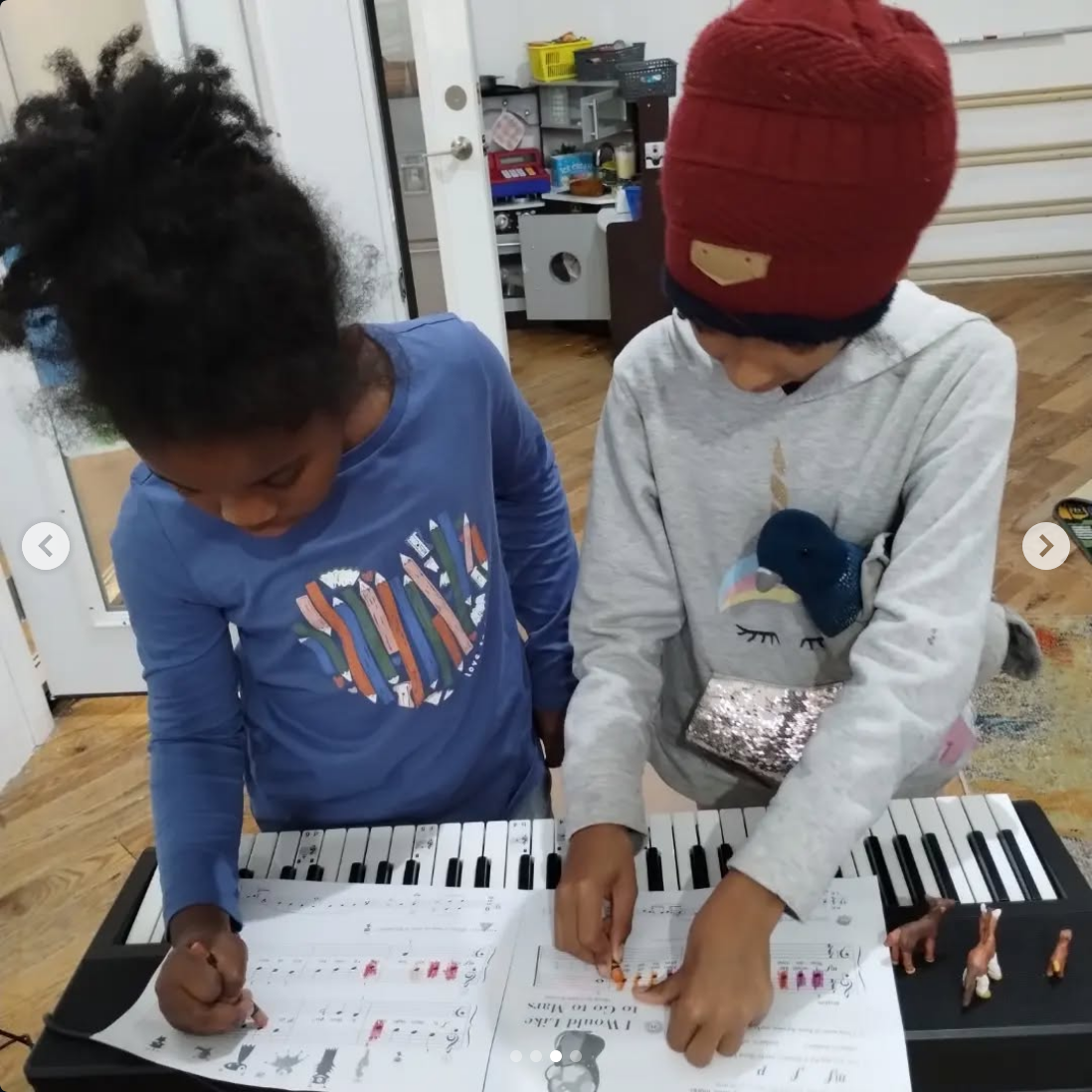 Two children are standing at a keyboard, practicing music from sheet music on the stand.