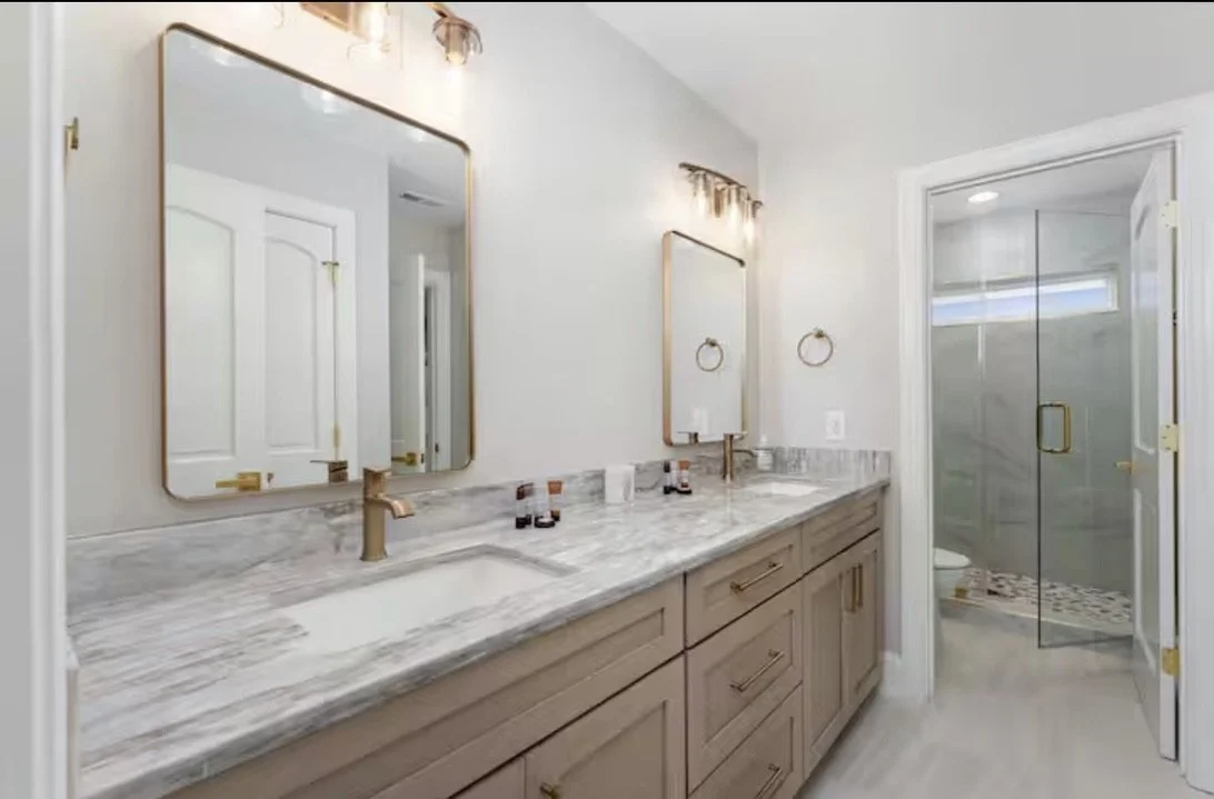 Luxury coastal bathroom design in Kure Beach NC with custom vanity, stone countertops, brass fixtures, and soft neutral finishes.