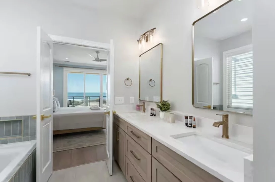 Bathroom finish selections for this luxury beach house in Kure Beach feature warm cabinetry, natural stone countertops, brass fixtures, and timeless tile selections, creating a clean and elevated coastal retreat.
