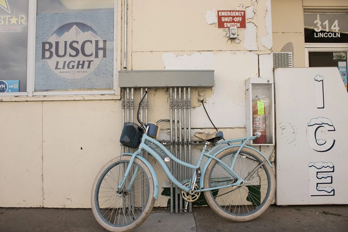 A light blue bicycle parked against a wall near a fire safety cabinet and an emergency shut-off switch with peeling paint.