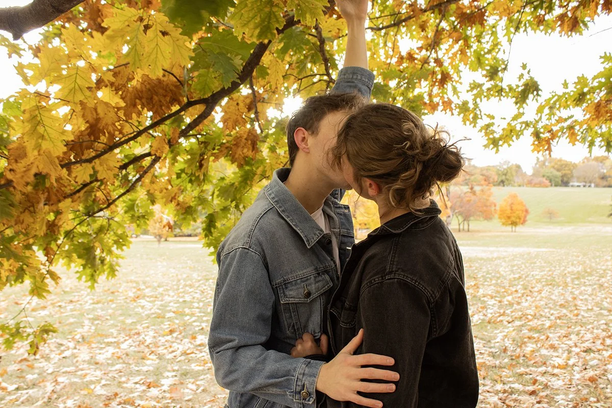 A couple sharing a kiss under a tree with autumn leaves.