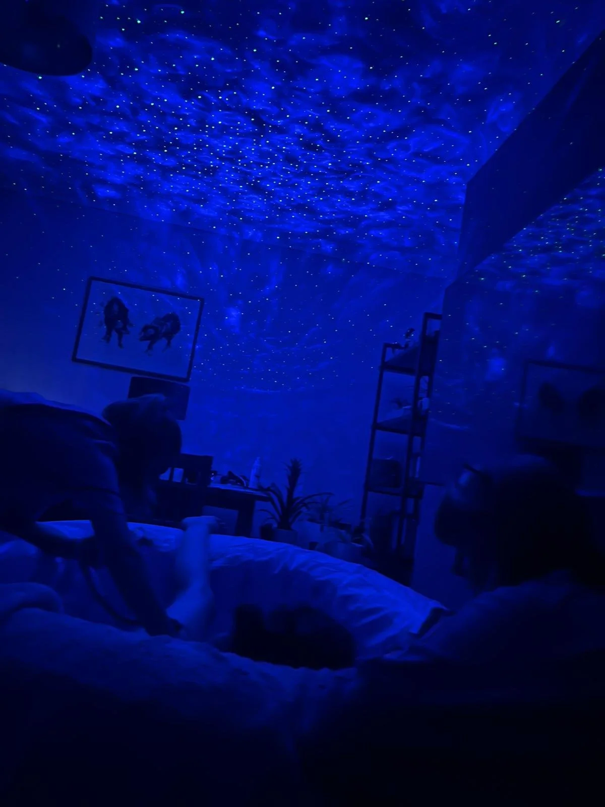 A labouring woman in birthing pool in living room, her mum watching over her and a midwife checking her babies heartbeat. The image is blue and dark from the lights in the room.