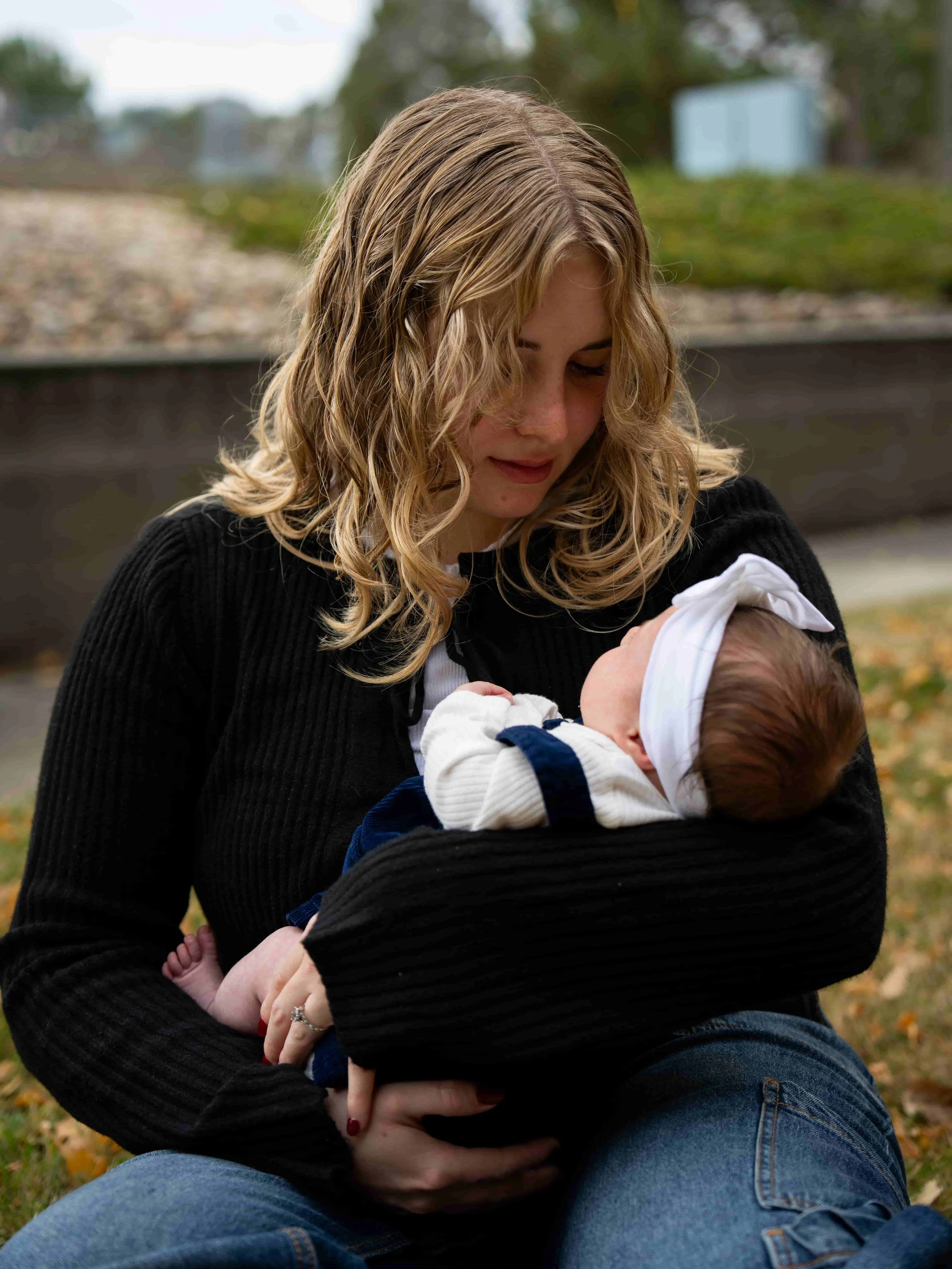 A woman with blonde hair holding and looking down at a baby outdoors