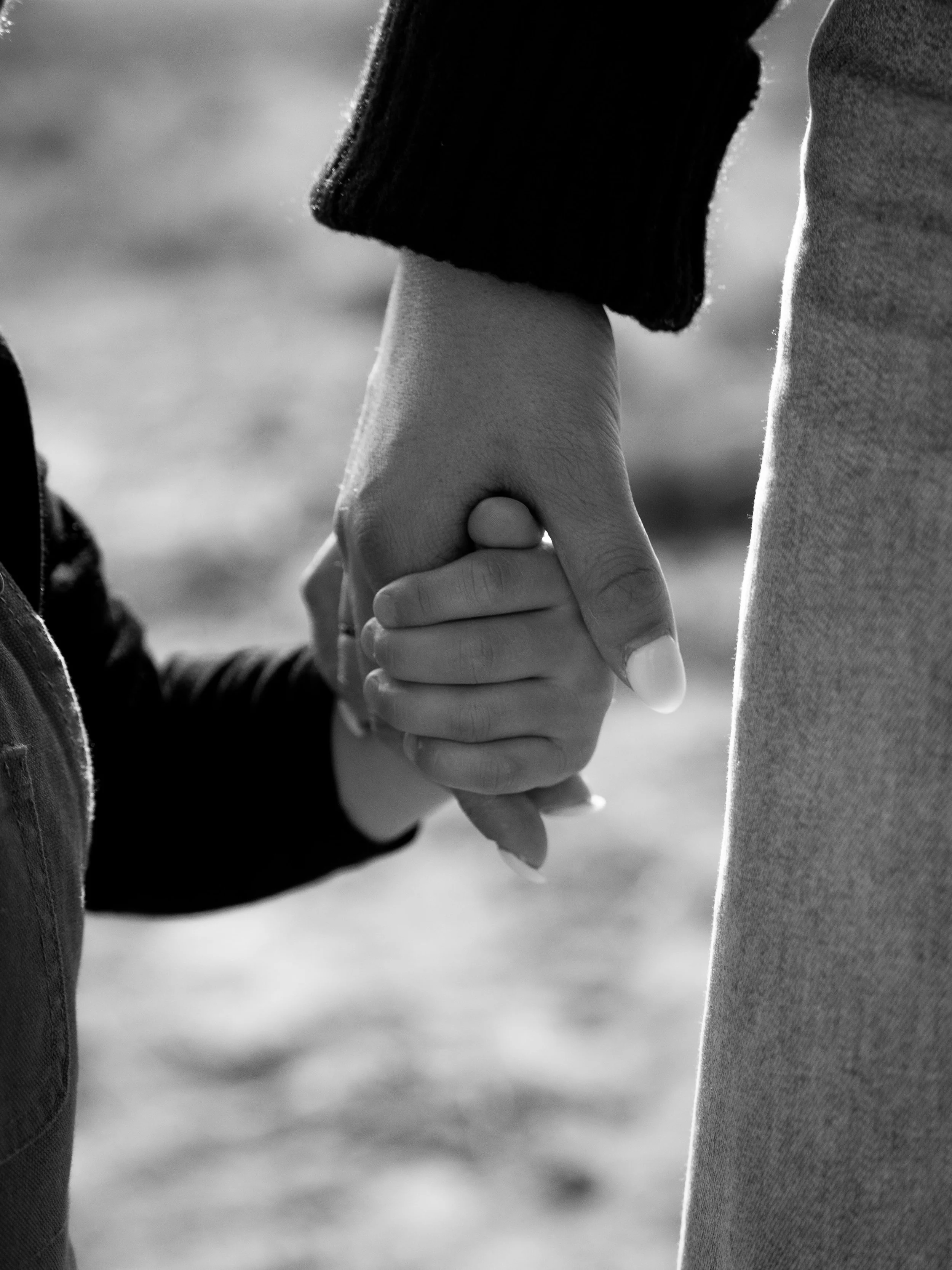 A close-up of two people holding hands, one child and one adult, in black and white, outdoors.