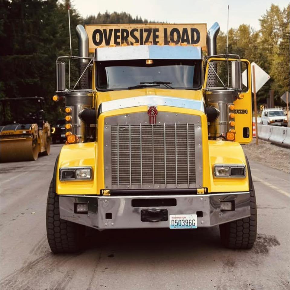 Front view of a large yellow dump truck with a sign that says 'Oversize Load' on top.