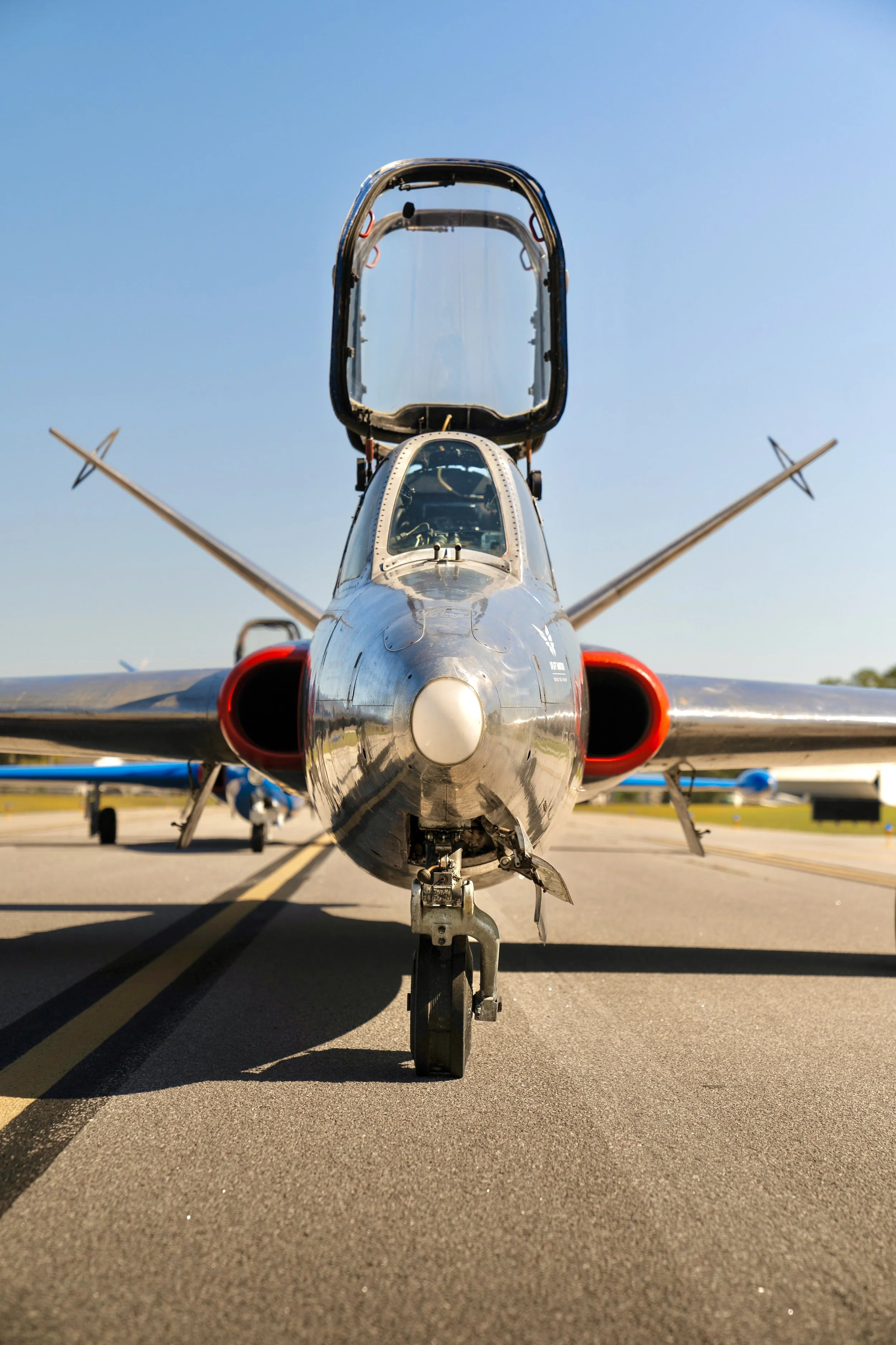 Front view of a military aircraft parked on the tarmac with a clear blue sky.