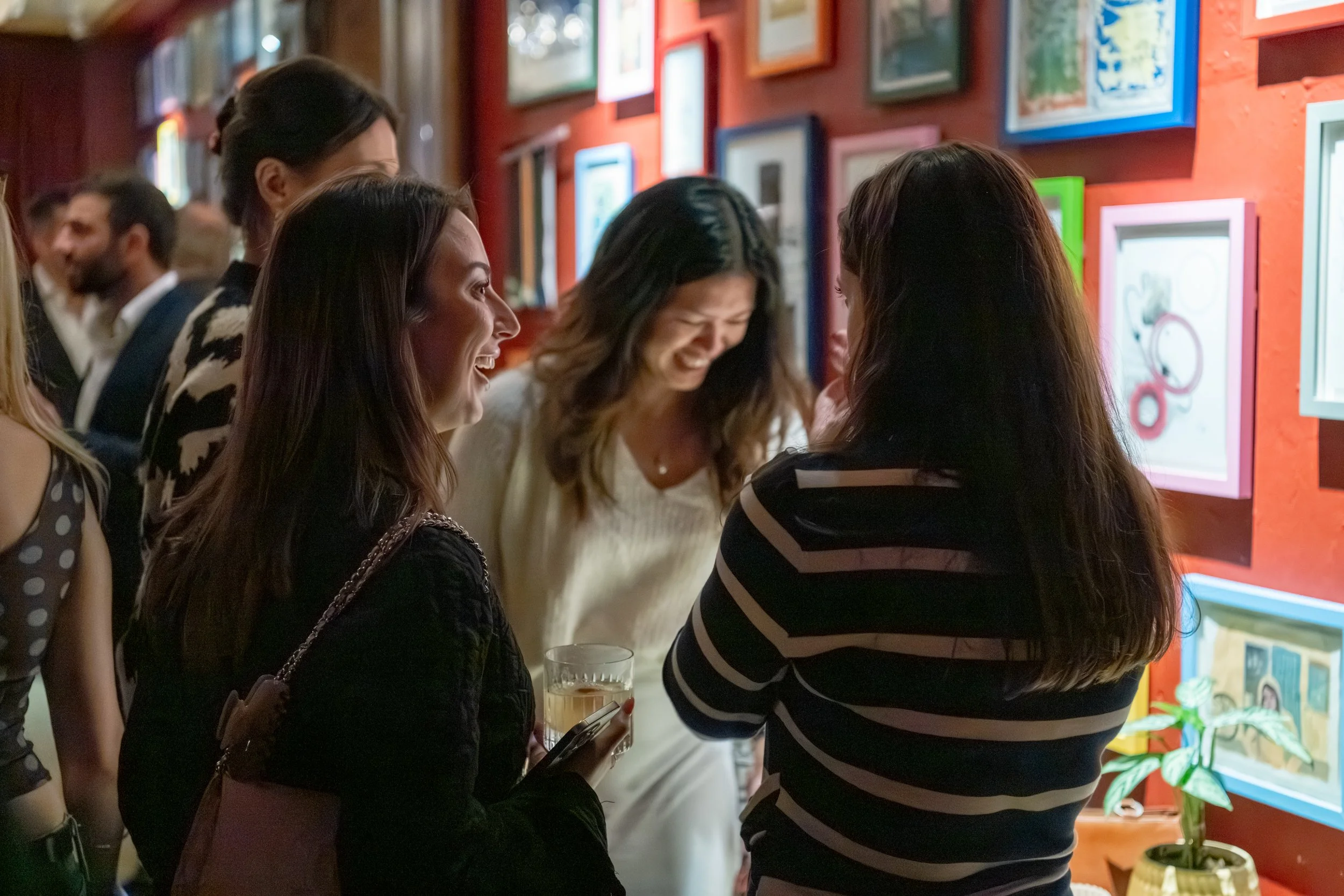 Group of women at a business event with art on the walls, engaging in conversation and smiling.