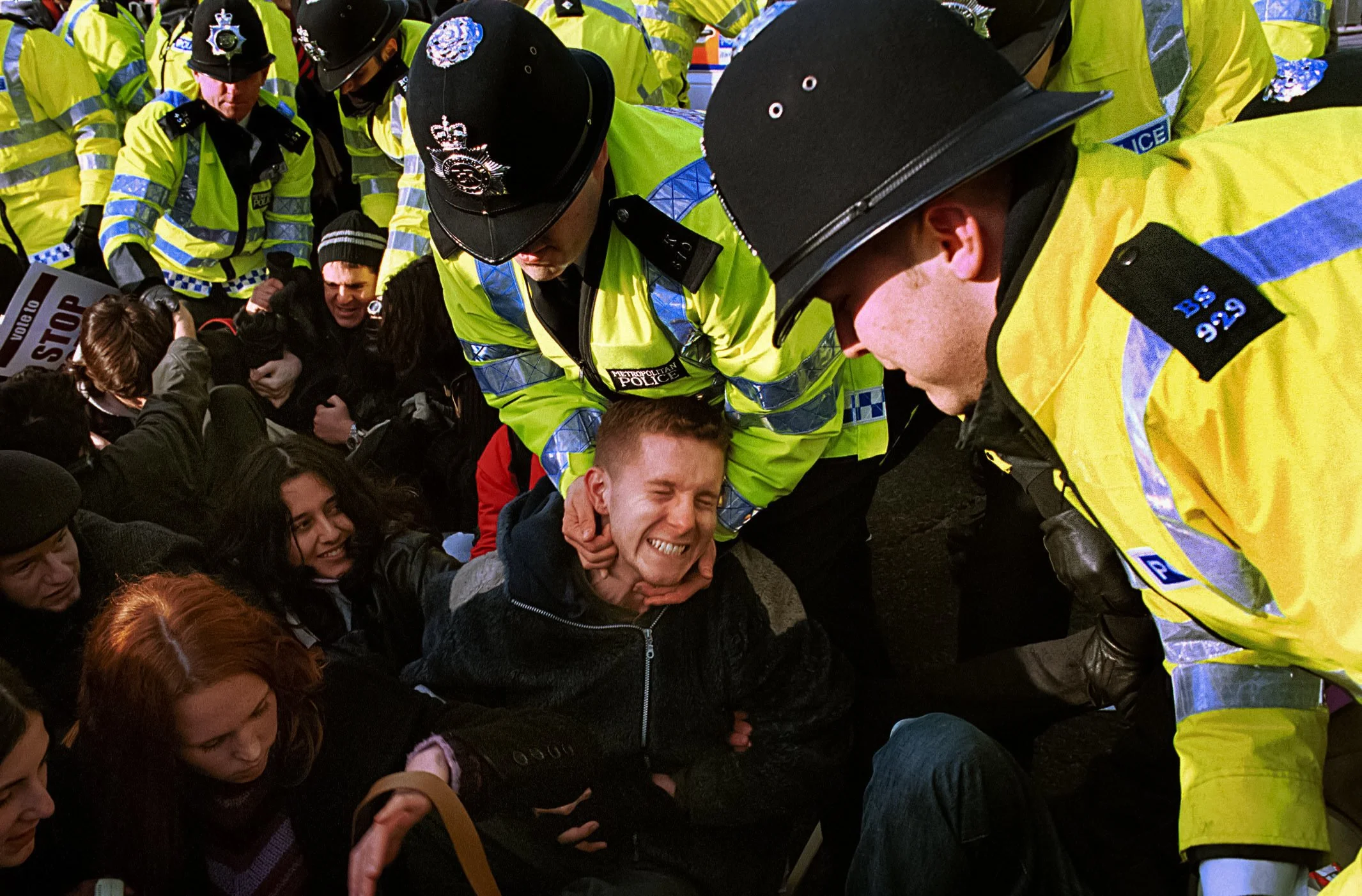 Police officers arresting a protester during a demonstration, with a group of bystanders observing.