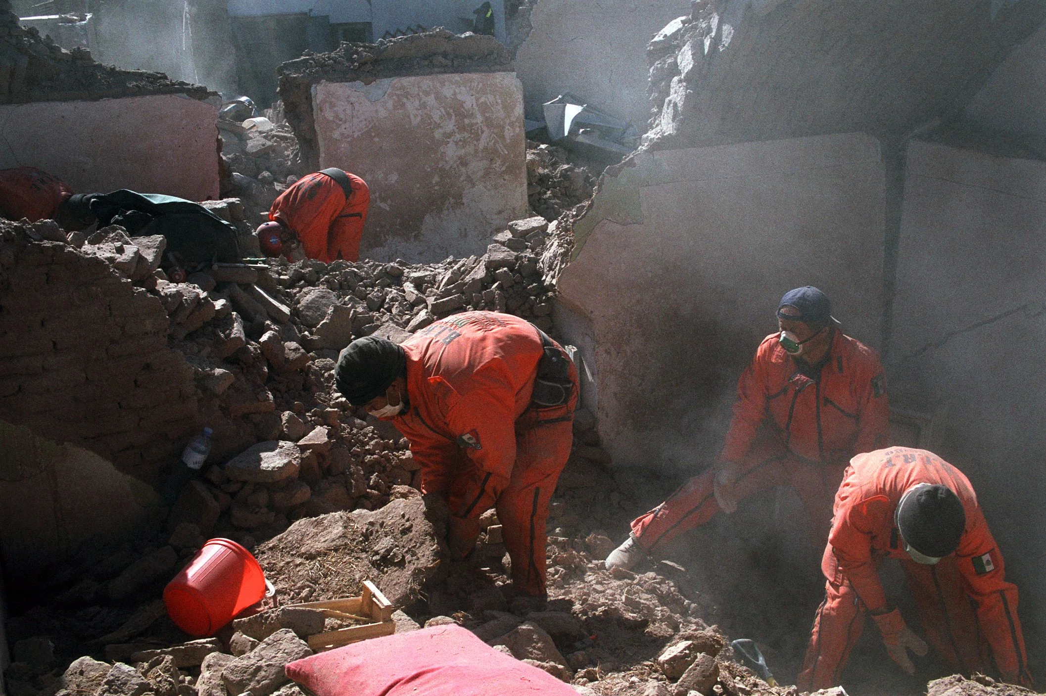 Rescue workers in orange uniforms searching through rubble and debris from a collapsed building.