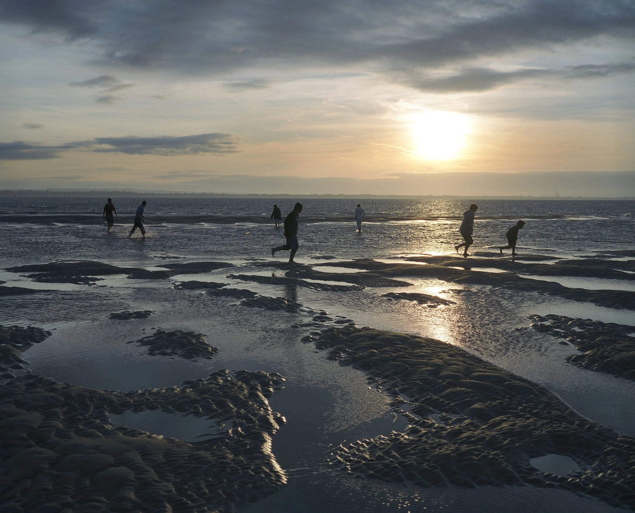 People walking and running on a beach during sunset with water reflecting the sky.