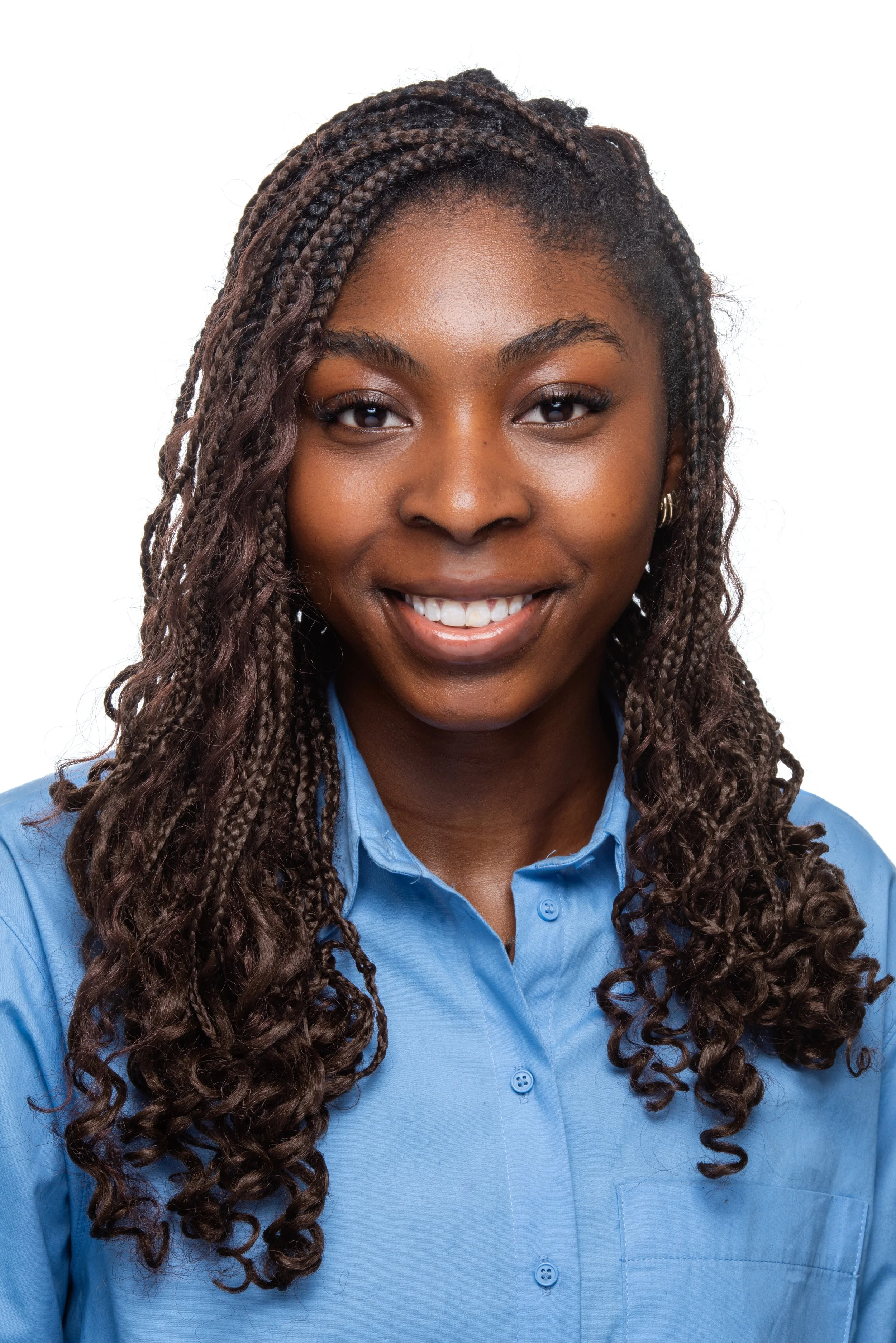 A smiling dark skinned woman with long twisted hair wearing a blue button-up shirt against a white background.