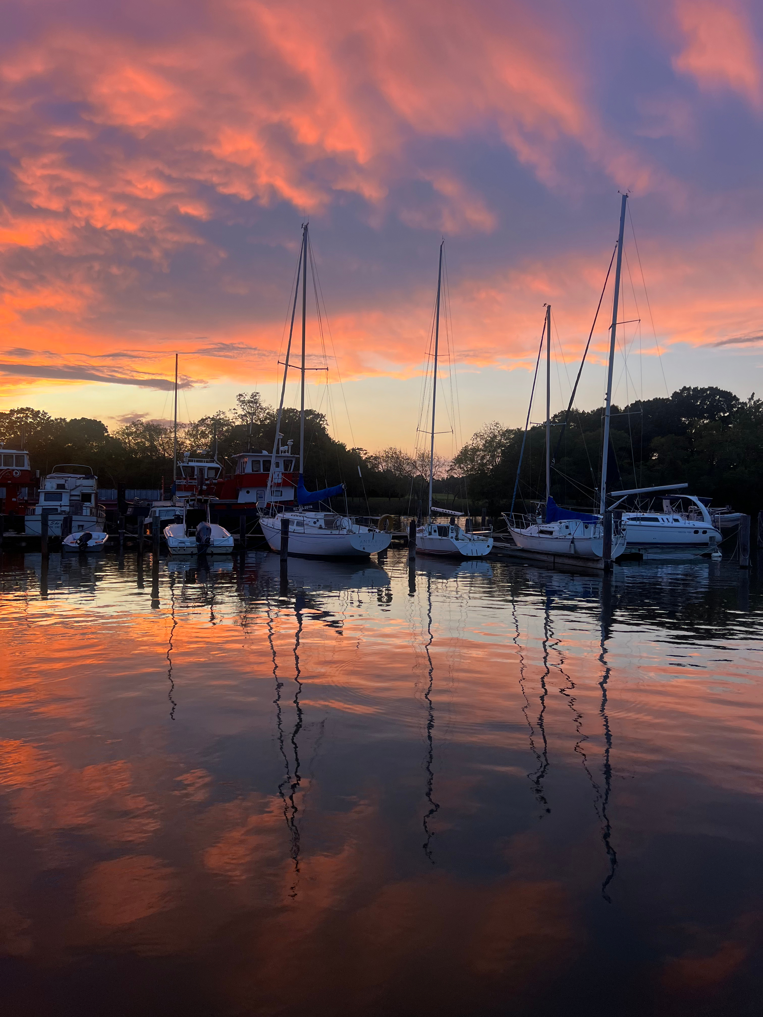Lerch Creek at sunset with sailboats and yachts docked, reflecting the colorful sky with orange, pink, and purple clouds on the water.