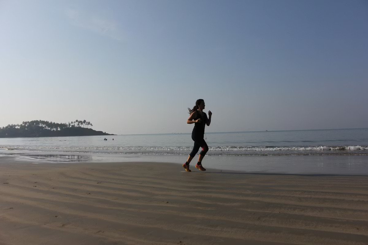 A woman jogging on a sandy beach near the ocean during daytime.